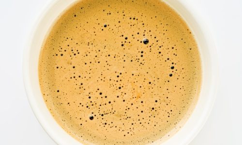 Cappuccino creamy milk foam texture in a white cup. Top view on white background. Design element.